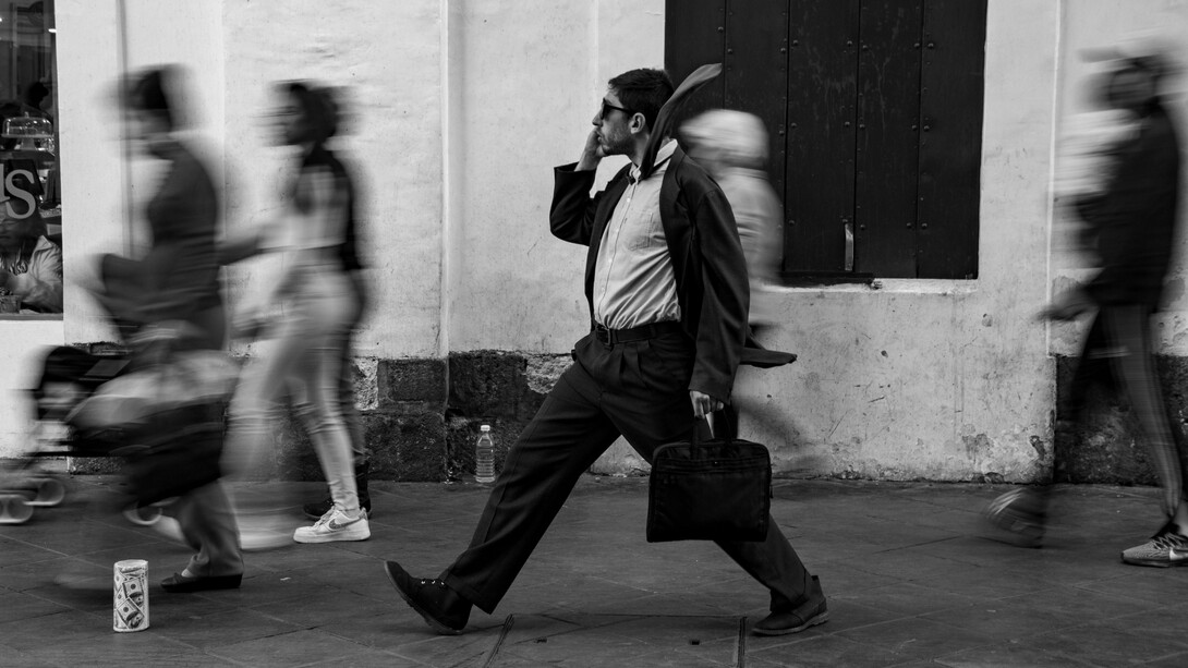 A focused man moving through a blur of rushing pedestrians, representing the modern pressure to stay constantly occupied