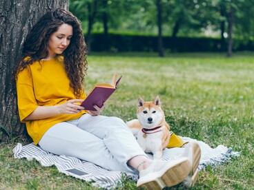 A woman relaxing under a tree with an open book while her dog sits beside her, reflecting the importance of slowing down to nourish the mind