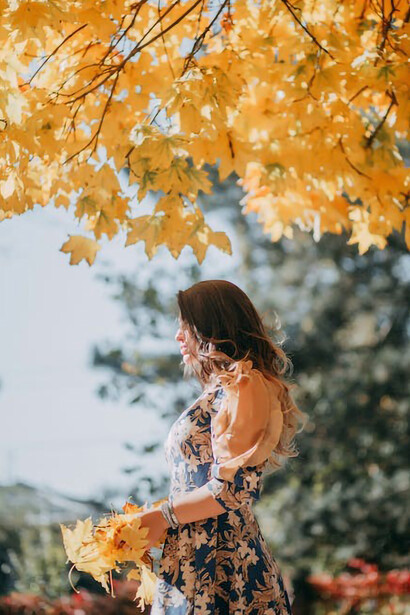 A photograph captures the serene beauty of a woman gracefully holding a handful of autumn leaves, embodying the essence of the season