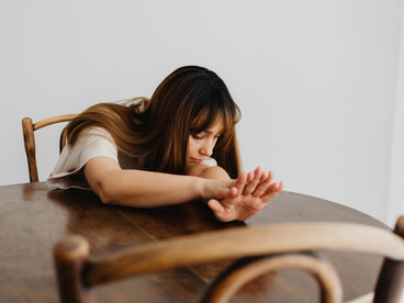A woman leans on a table, looking overwhelmed and deep in thought