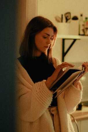 A woman in a white sweater is reading a book at home