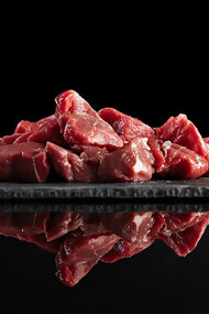 Pieces of raw, fresh meat displayed on a black stone board, beautifully mirrored for a striking presentation