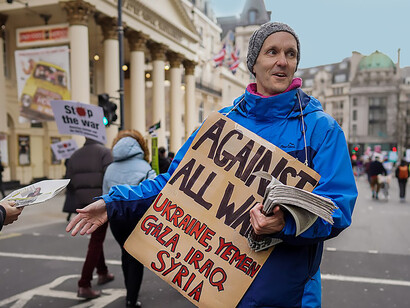 A photo of a pro-Ukraine demonstration in Trafalgar Square, London, UK, featuring a man holding a banner that reads: "Against All War"