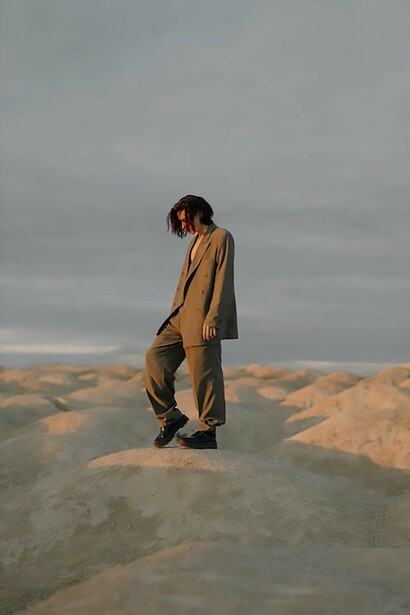 A man, dressed in a sleek gray long-sleeve shirt and pants, stands gracefully on a rustic brown rock
