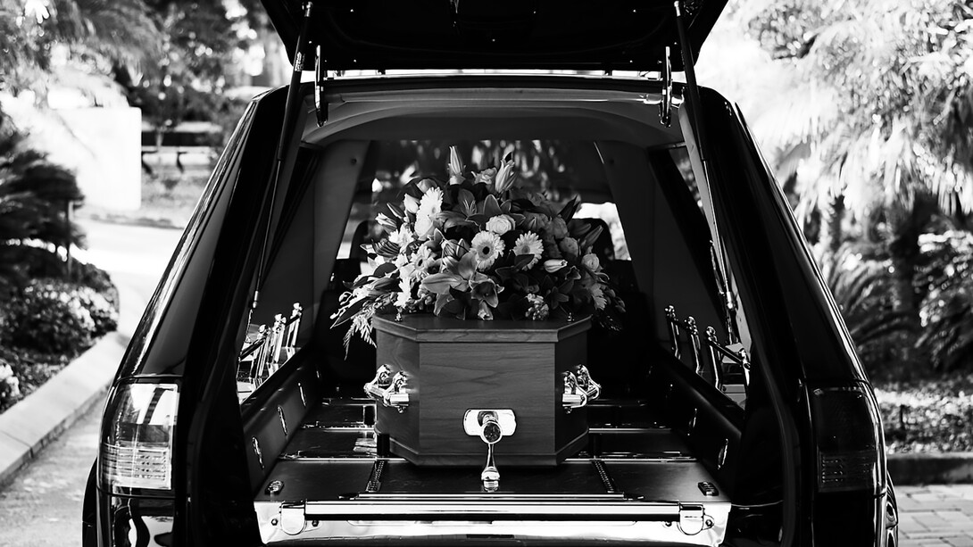 A grayscale photo of a car adorned with flowers, part of a solemn funeral procession