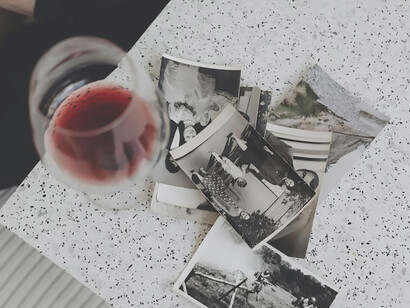 With a wine glass in hand, the woman gazes at the photos, her eyes reflecting a poignant blend of sadness and longing