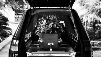 A grayscale photo of a car adorned with flowers, part of a solemn funeral procession