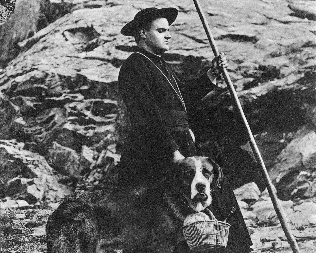 Cleric with dog carrying a basket, poses for the camera. Great St Bernard Hospice VS, around 1900–1910.
© Hospice du Grand-Saint-Bernard/Médiathèque Valais.