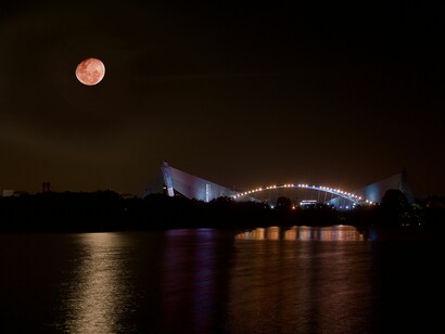 Lighted arch bridge and body of water under red moon