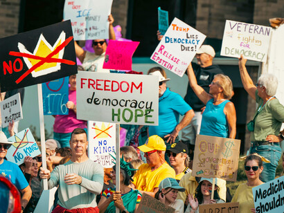 Protesters carrying signs and American flags gather during a peaceful rally in the United States, calling for the protection of democratic rights and freedoms