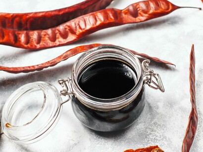 Xarope de alfarroba em frasco de vidro com vagens de alfarroba e sementes. No contexto da indústria alimentar emprega-se em confeções várias, como comida pré-cozinhada, comida para bebé, molhos variados, queijo-creme, iogurtes, gelados, sobremesas lácteas, refrigerantes, produtos de panificação, pastelaria diversa e fibras alimentares
