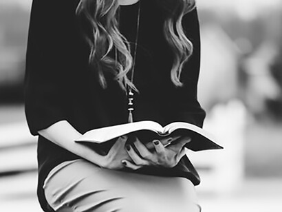 A greyscale image of a woman sitting on a rock, reading a book
