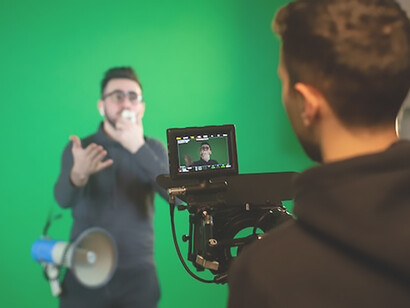 In the spotlight, a person stands before the camera, articulating their message with poise while holding a microphone, the versatile green screen behind them ready to transform the scene in the process of an exciting filming endeavor