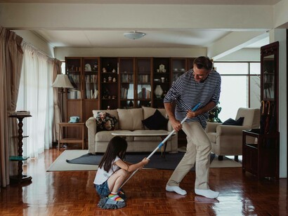 Man happily sweeps the floor with his daughter