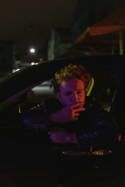 A man smoking a cigarette out the window of a car at night 