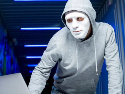 A hacker in a mask and hoodie working on a computer
