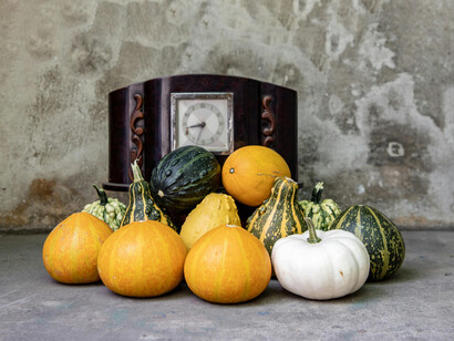 Different types of gourds and pumpkins on a concrete floor next to a wooden clock