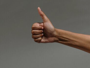Uma mão faz o tradicional gesto de aprovação com o polegar levantado. Mesmo sem palavras, um movimento corporal pode transmitir uma mensagem reconhecível e participar de um ato de comunicação