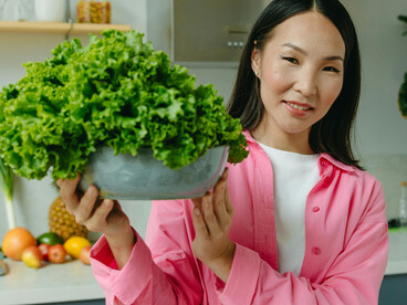 A woman carrying a bowl of fresh lettuce, representing a plant-based diet, vegan lifestyle, and healthy eating