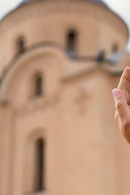 A woman with open hands stands beside a religious building during a spiritual visit