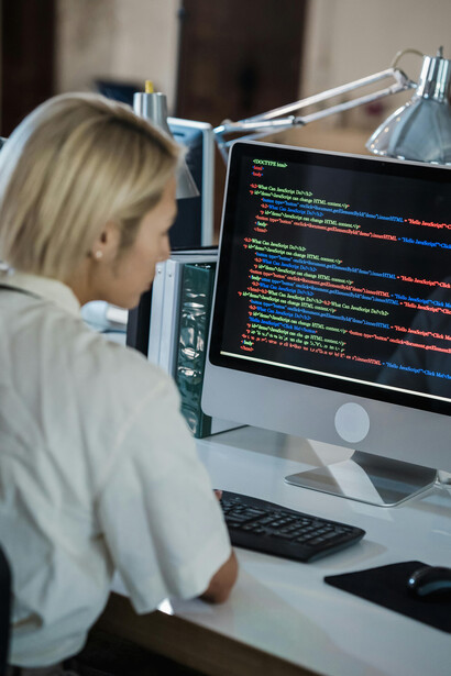 Vertical composition of a woman working in an office, looking at a computer screen displaying lines of multicolored code