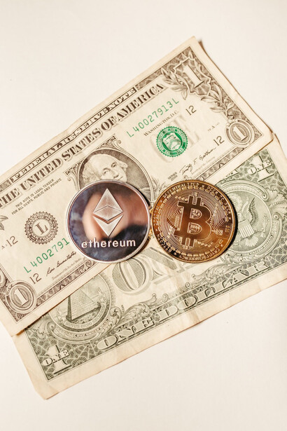 A Bitcoin and Ethereum cryptocurrency coin resting on a stack of cash money