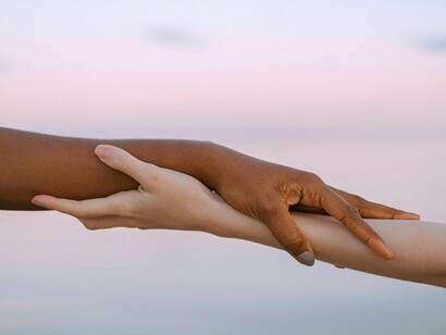 Two hands, one darker and one lighter, clasp each other against a soft, pastel sky, symbolizing unity amidst diversity and the importance of connection