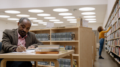 Pessoas em uma biblioteca estudando e escolhendo livros de teoria literária