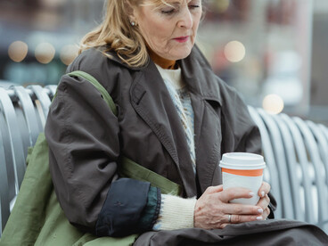 Melancholic woman sitting alone on an urban bench, holding a takeaway coffee and lost in thought amid the city around her