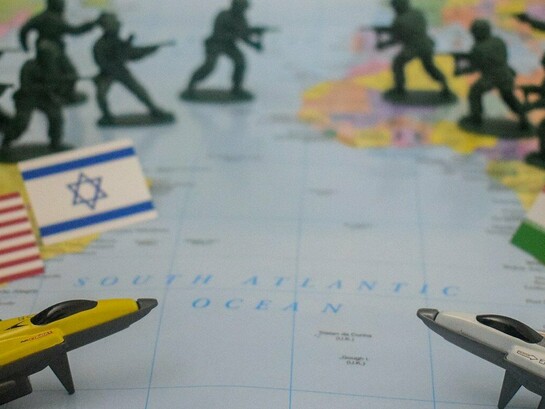 Soldados de brinquedo e bandeiras dos Estados Unidos, Israel e Irã sobre um mapa-múndi representam a disputa militar e geopolítica que envolve as três potências. A escalada no Oriente Médio transforma uma rivalidade regional em uma crise com potencial para afetar alianças, mercados e o equilíbrio estratégico internacional