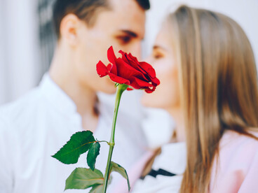 A rose held delicately as a couple shares a moment behind it, highlighting romance, drama, and the stakes of reality dating shows like Bachelor