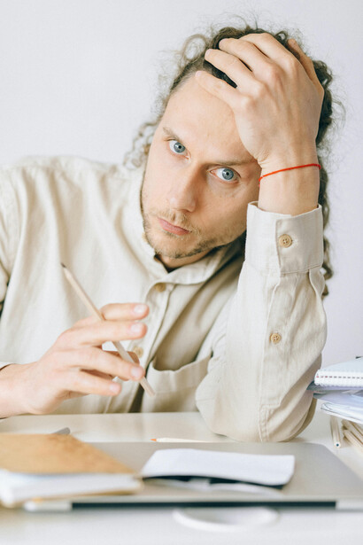 Young man showing signs of stress and emotional fatigue at work, surrounded by notes on his desk, reflecting workplace burnout and Gen-Z anxiety