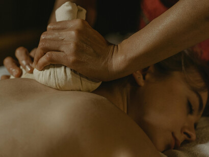 A close-up of hands performing Ayurvedic massage with fabric herbal pouches, part of the detoxifying Panchakarma treatment
