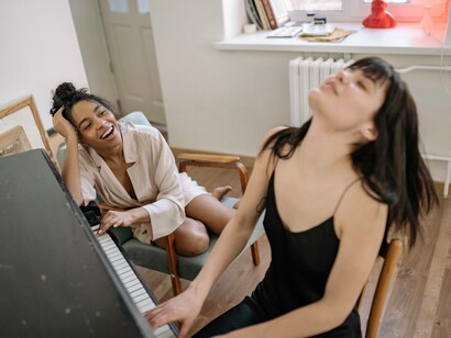 A woman on the piano playing with flair as another laughs with appreciation