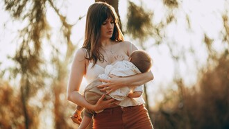 Mulher segura o bebê junto ao corpo em meio à floresta, sob a luz suave do fim de tarde. O vínculo entre mãe e filho está no centro da discussão sobre os benefícios e as características do leite materno