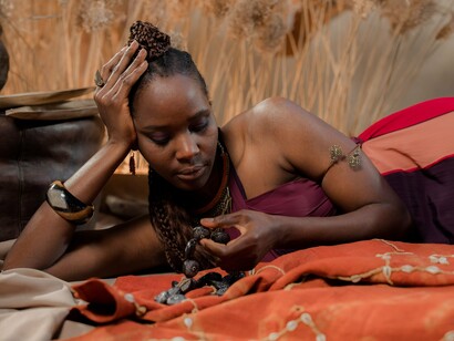 A woman laying down beside fabrics and heritage jewellery, reflecting the way culture carries layers of memory and meaning