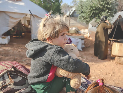In the Idlib Governorate of Syria, a heartwarming scene unfolds as a resilient young girl cherishes a toy amidst the challenges of life in a refugee camp