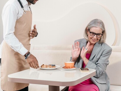 A waiter being hospitable offers a complimentary dish from the restaurant to a customer but she refuses bashfully 