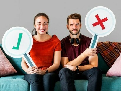 A cheerful couple sits on a couch, holding vote icons representing red and green flags