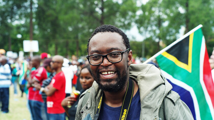 With the South African flag waving behind him, he embodies the spirit of unity and resilience in the fight for equity