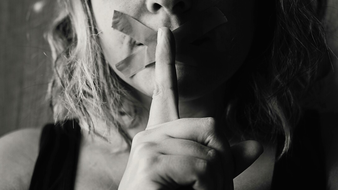 A woman places her finger on her already duck-taped lips