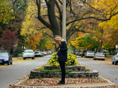 A teenage mother standing by a brown wooden fence, looking thoughtfully into the distance