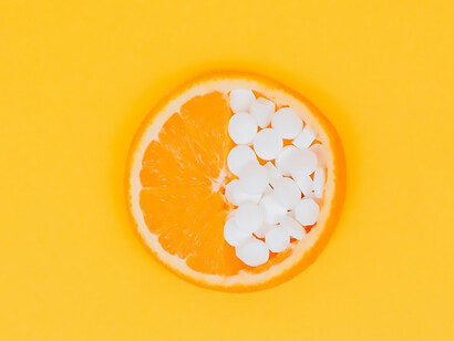 A burst of color emanates from a radiant yellow and orange background, where a succulent slice of orange and lemon coexists with an array of pills and vitamins