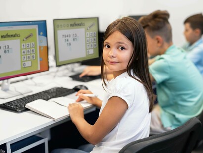 Una bambina che sta lavorando a un compito di matematica, con un quaderno aperto davanti a un computer su cui si vede un'attività didattica