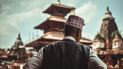 A Nepali man stands in the foreground, gazing at the majestic temple in Patan, Nepal, surrounded by the rich cultural architecture of the ancient city