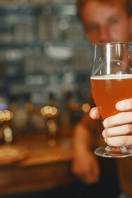 A man with a beer glass in his hand, sitting in a bar, enjoying pint of his beer
