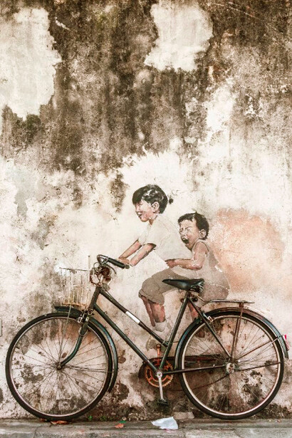 A girl and a boy riding a bicycle past wall art in George Town, Malaysia