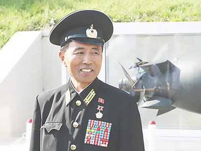 A North Korean naval captain serving as a guide stands next to the USS Pueblo in North Korea