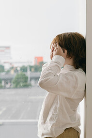 A child next to a window covers his eyes with his hands