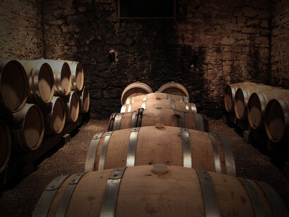 Brown wooden barrels are displayed against a rustic brown brick wall at Chateau Gigonan, a renowned producer in Châteauneuf-du-Pape, France